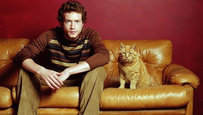 man sits next to cat on couch