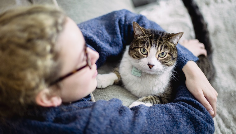 A girl wearing eyeglasses with her arms around her tabby cat