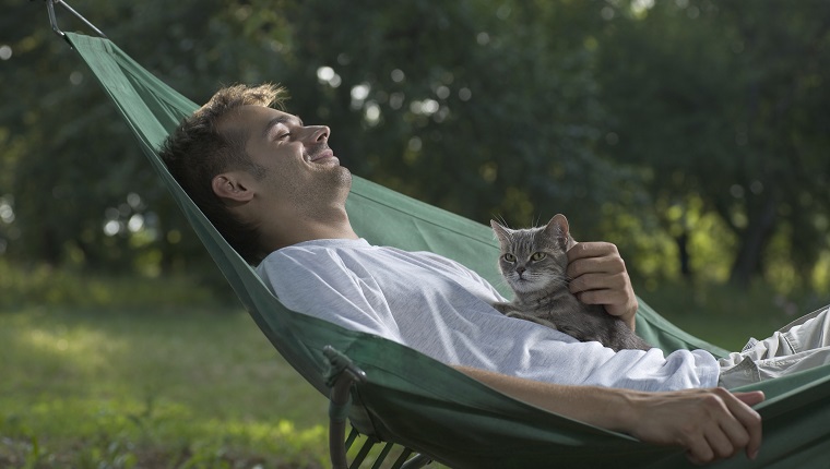 A man lying in a hammock petting a cat