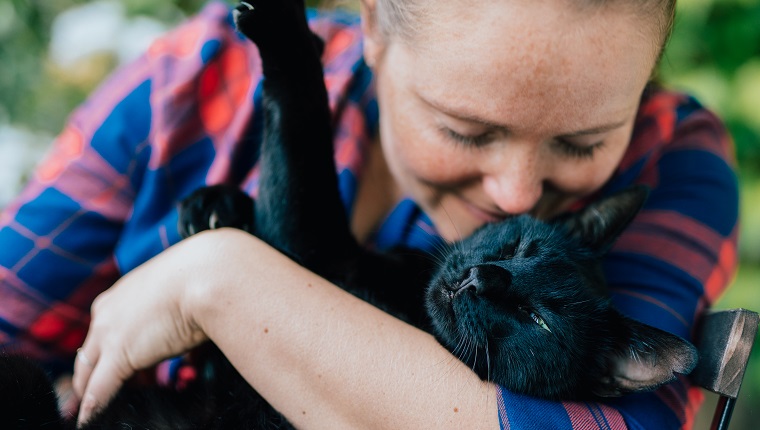 Portrait of blondhaired woman hugging her black cat outdoor.