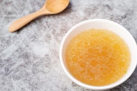 Bowl of chicken broth on table with wooden spoon.