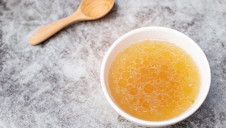 Bowl of chicken broth on table with wooden spoon.