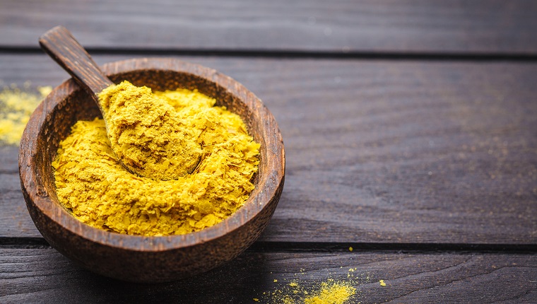 Nutritional yeast in a wooden bowl, copy space, dark background, copy space. Healthy vegan food concept.